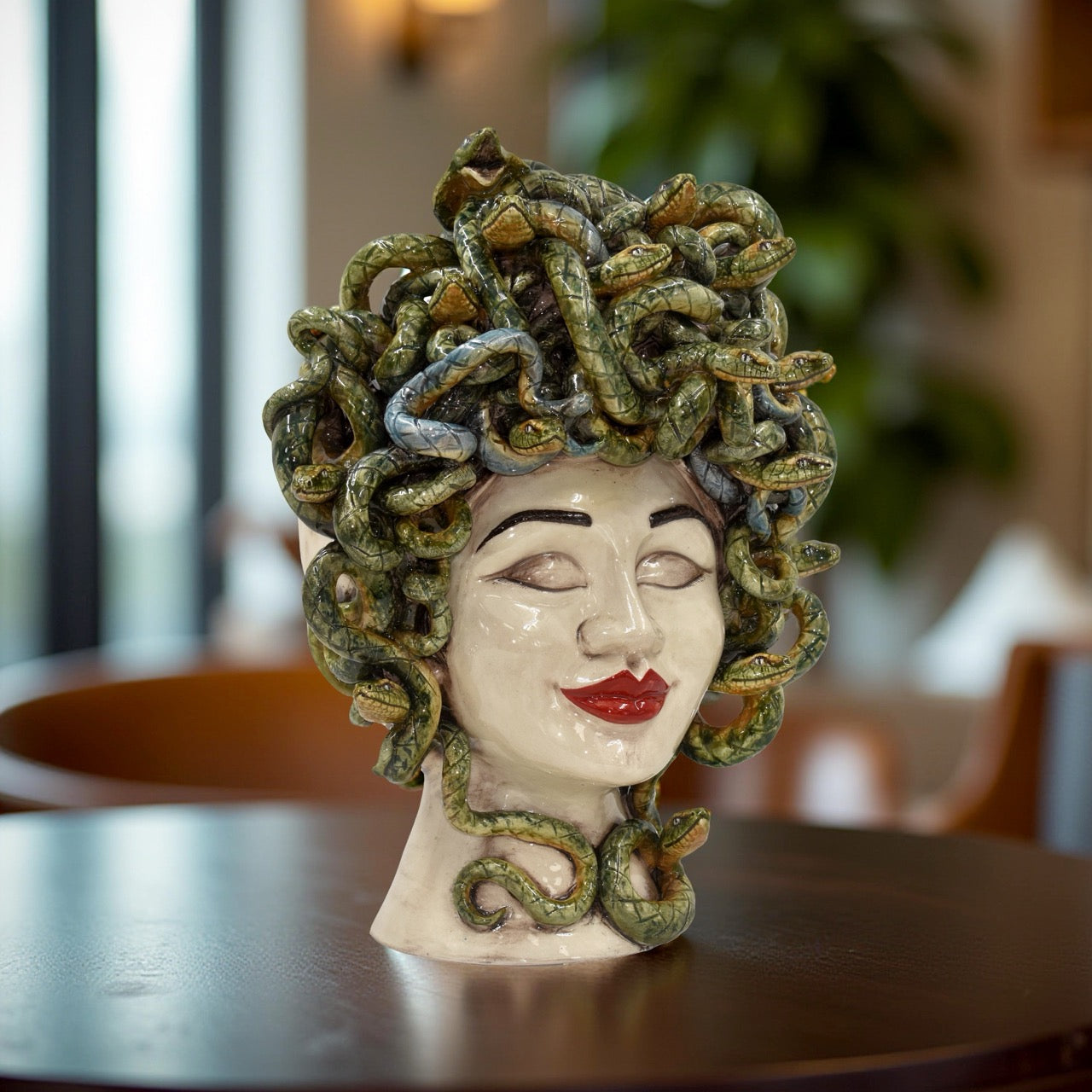 Handcrafted ceramic Medusa female head with red lips and green snakes on display