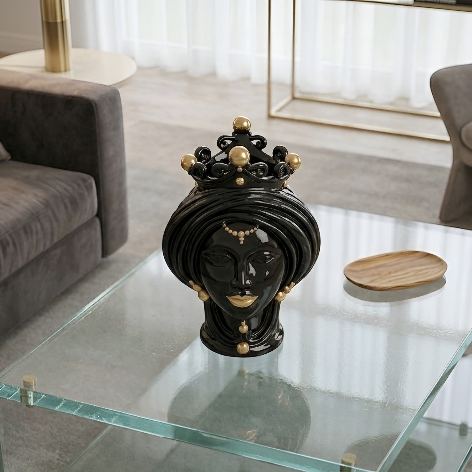 Black and gold Teste di Moro ceramic head sculpture with crown, displayed on glass table in modern living room