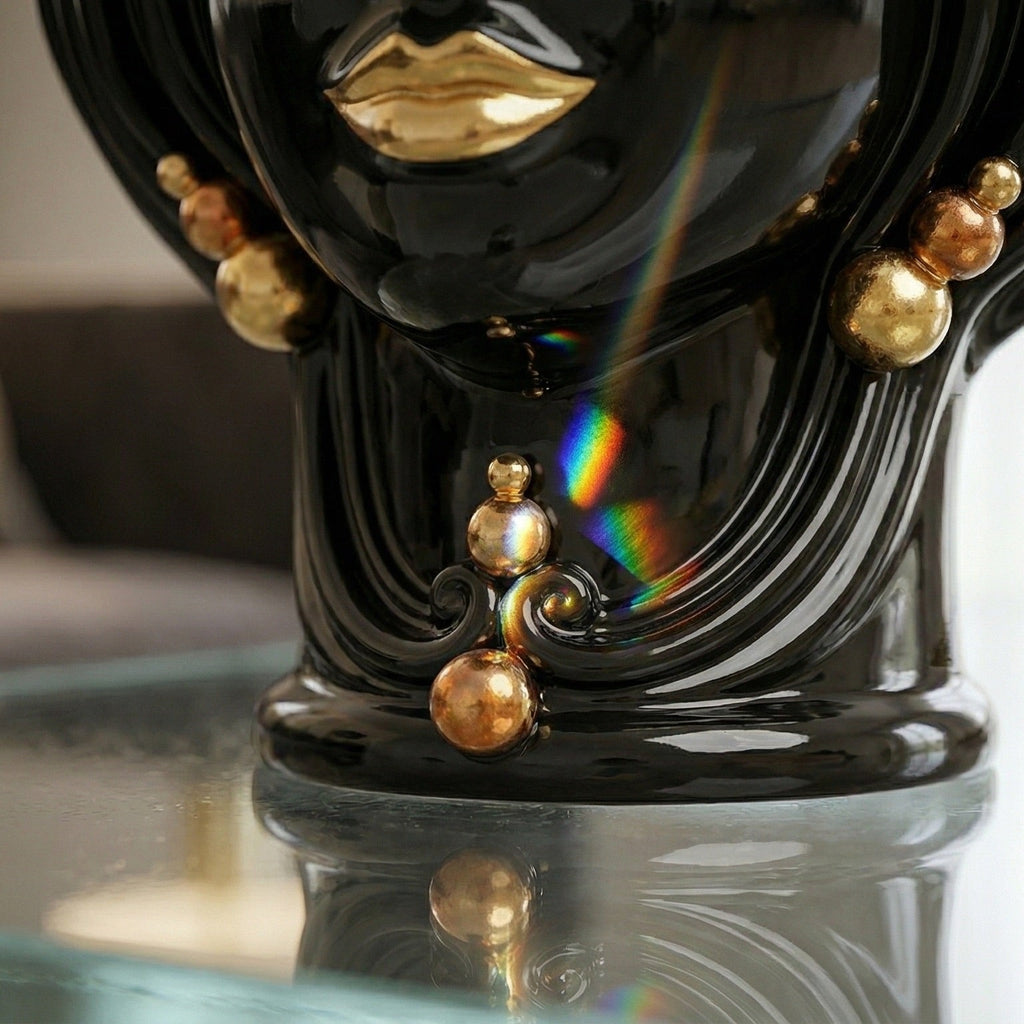 Glossy black Testa di Moro vase with gold lips and beads, reflecting rainbow light on glass surface