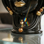 Glossy black Testa di Moro vase with gold lips and beads, reflecting rainbow light on glass surface