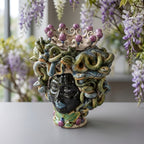 Handcrafted Teste di Moro vase with Medusa serpent hair, crown, and vibrant glaze, set against wisteria blooms.