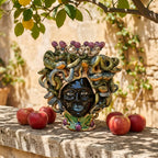 Handmade Teste di Moro ceramic with snake hair, purple grapes, and apples on stone ledge under lemon tree