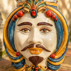 Handmade Teste di Moro ceramic face with vibrant blue, yellow, and red details, traditional Sicilian decor.