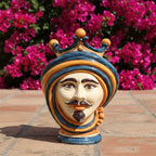 Handcrafted Teste di Moro ceramic head with crown, vibrant blue and gold, set against pink flowers