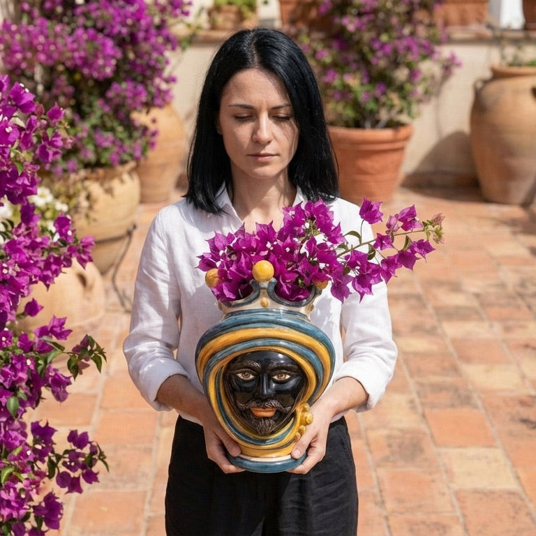 Woman holding a handcrafted Testa di Moro vase with vibrant purple flowers, showcasing Sicilian ceramic art.