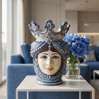 Handmade ceramic Testa di Moro with blue crown, displayed on white table beside blue peonies in modern living room.