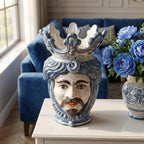 Handmade ceramic Teste di Moro vase with blue crown, displayed on white table beside blue flowers in modern living room