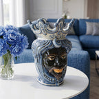Handmade Teste di Moro ceramic vase with blue crown, displayed on white table beside blue flowers in modern living room
