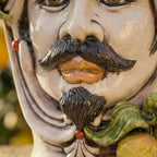 Handcrafted Teste di Moro ceramic face with mustache, green leaves, and fruit, blending tradition and modern design.