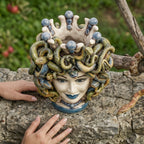 Handmade Medusa Testa di Moro ceramic vase with snakes, blue accents, and crown, displayed outdoors on stone.