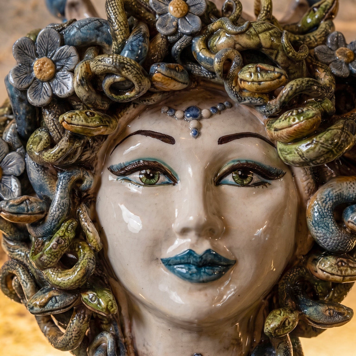 Nahaufnahme des Medusenkopfs mit Blumen: grüne Augen, blaues Diadem und blaue Lippen