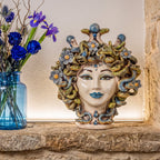 Medusenkopf mit Blumen auf einer Steinablage neben einer Vase mit blauen Iris