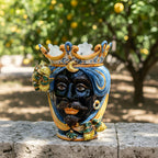 Handcrafted Teste di Moro ceramic vase with crown, vibrant colors, and lemon accents, set outdoors.