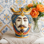 Handcrafted Teste di Moro vase with crown, blue hair, mustache, and red beads, set against patterned tiles