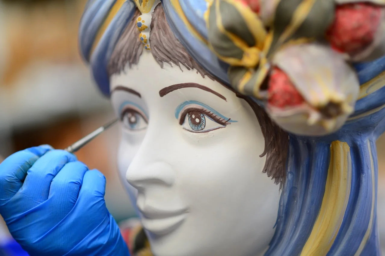 Hand-painted Teste di Moro ceramic, artisan adding eye detail with brush, blue turban, floral crown