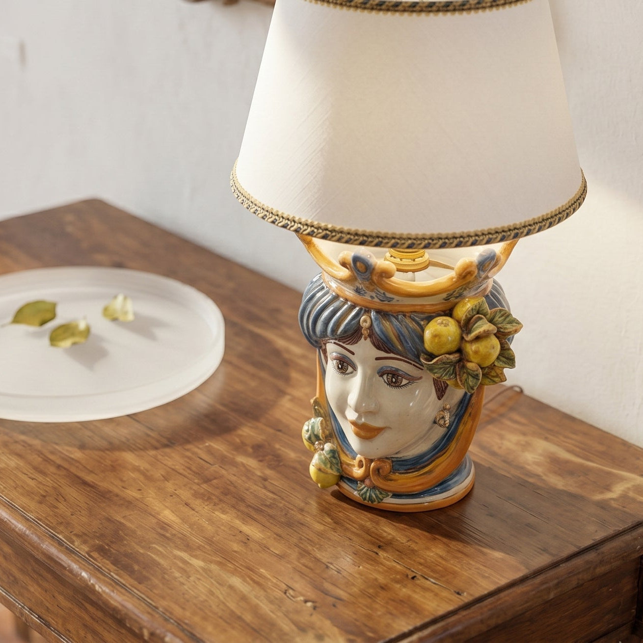 Hand-painted Teste di Moro table lamp with ceramic face, fruit accents, and cream shade on wood surface