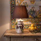 Handmade Teste di Moro ceramic lamp with a dark shade on a rustic wooden table.