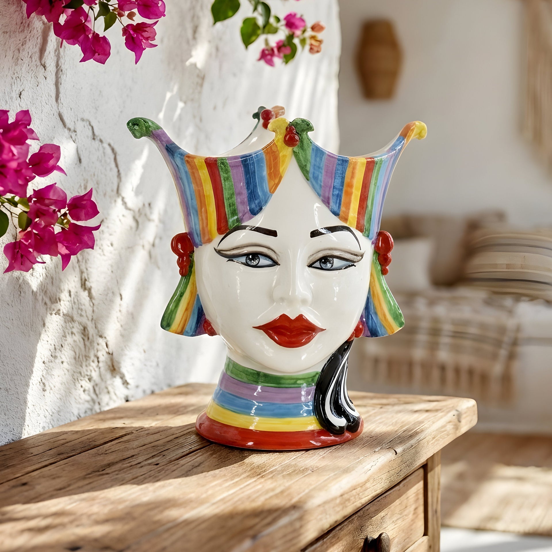 Colorful ceramic Teste di Moro vase with rainbow stripes, displayed on wooden table near pink flowers