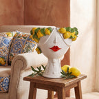 Handmade Teste di Moro vase with lemon crown, red lips, on wooden table beside lemons and olive branches