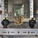 Black Teste di Moro vases with gold accents flanking a golden rooster sculpture on a console table