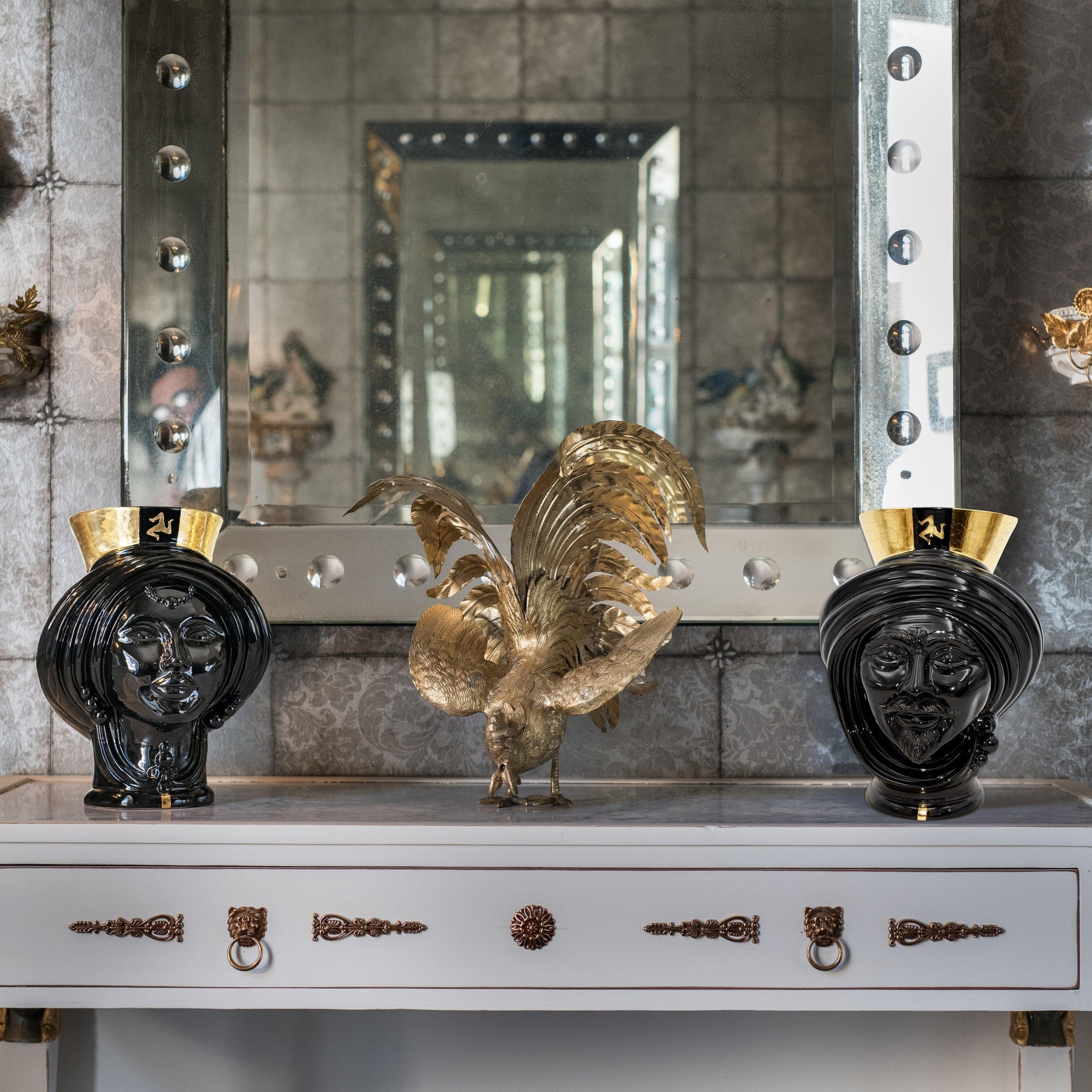 Black ceramic Teste di Moro vases with gold accents flanking a golden rooster sculpture on a console table
