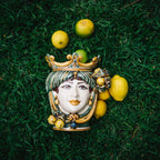 Handmade Sicilian Testa di Moro ceramic face with crown, surrounded by lemons on grass