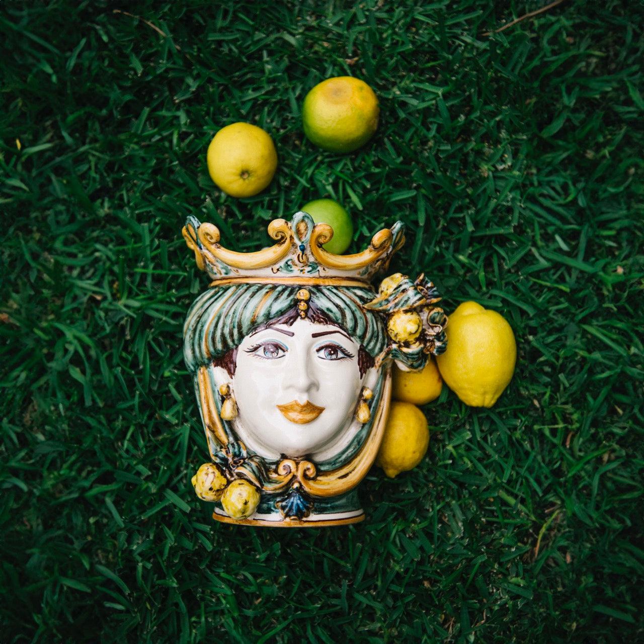 Handmade Sicilian Testa di Moro ceramic face with crown, surrounded by lemons on grass