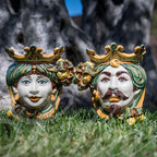 Handcrafted Teste di Moro ceramic faces with crowns, vibrant colors, set on grass