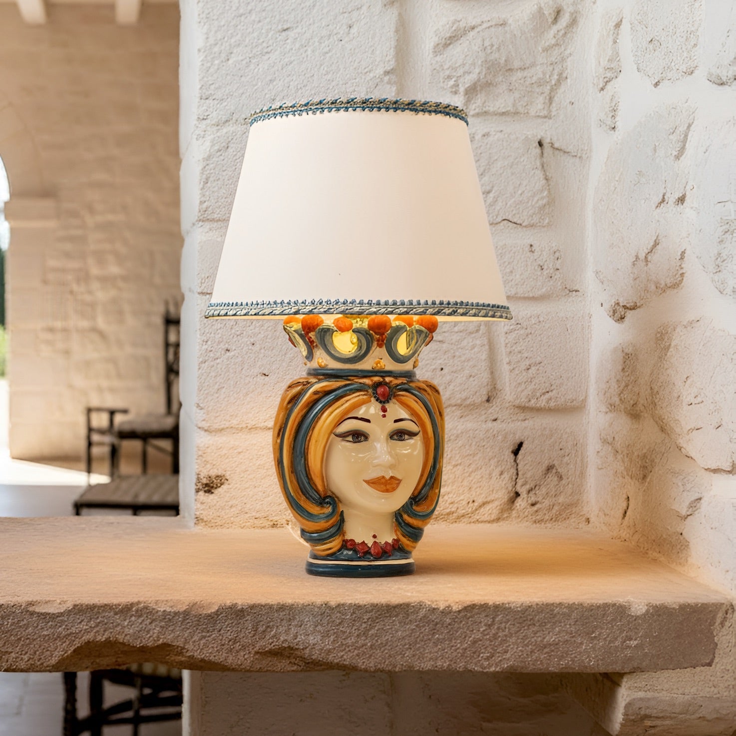 Handmade Sicilian Testa di Moro table lamp with colorful ceramic face, crown, and cream shade on stone ledge