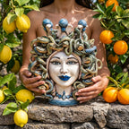 Handmade Teste di Moro ceramic with snake crown, held amid lemons and oranges, blending tradition and modern design.