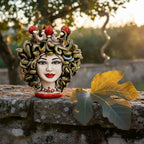Handmade Teste di Moro ceramic with snake hair, red accents, on stone ledge with fig leaf, sunset backdrop
