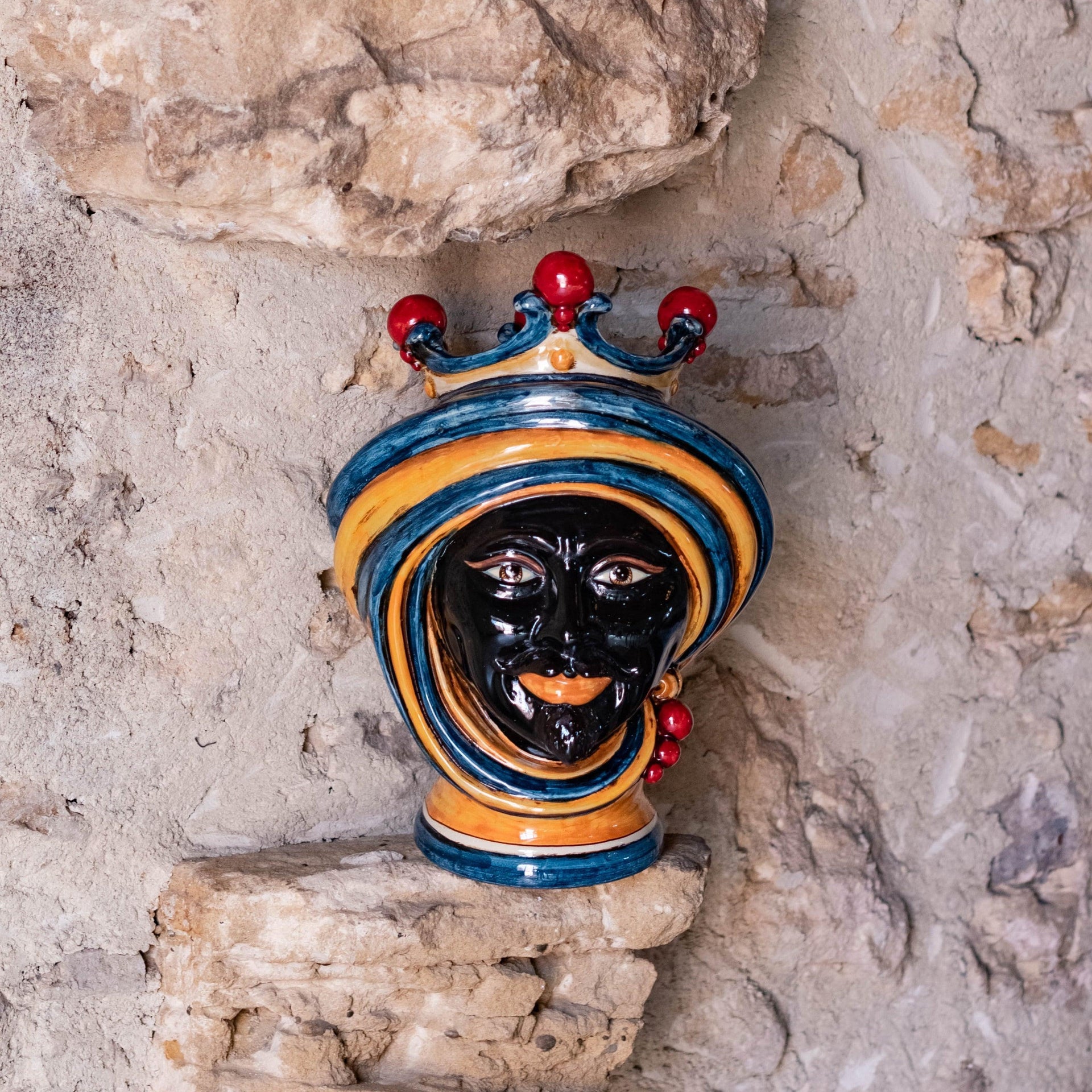 Handcrafted Moro ceramic head in blue and orange with crown on stone background