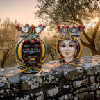 Handcrafted Teste di Moro ceramic statues, male and female, with ornate crowns, displayed on stone wall at sunset